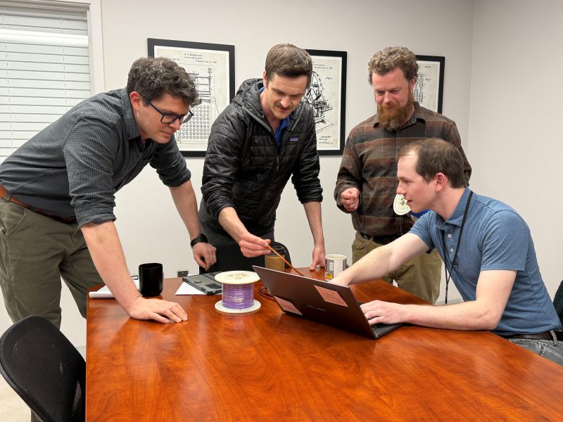 Four engineers around a table with laptop discussing cable samples